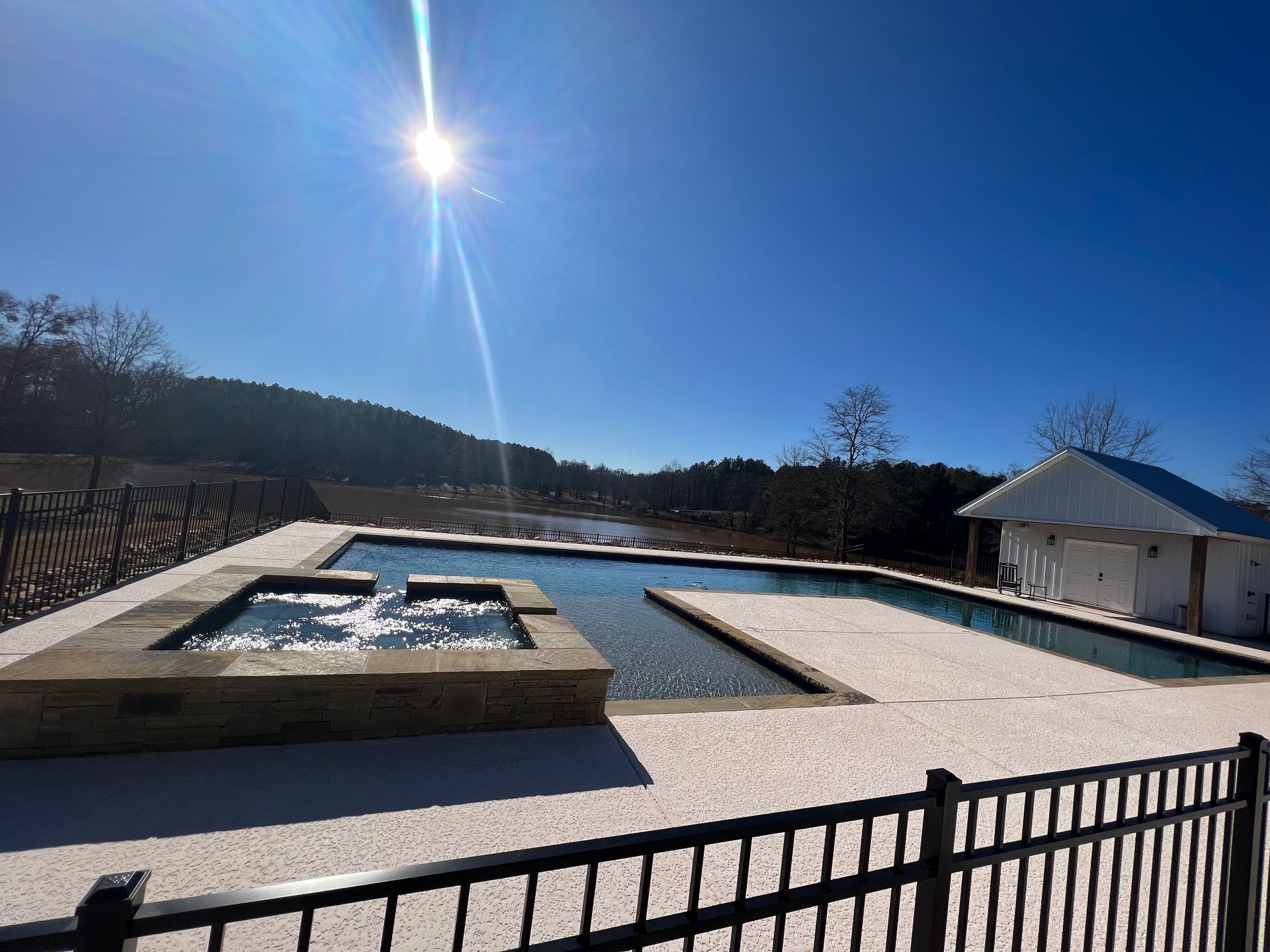 Pool and spa with jets, on a sunny day. Fence in foreground, hills in the background.