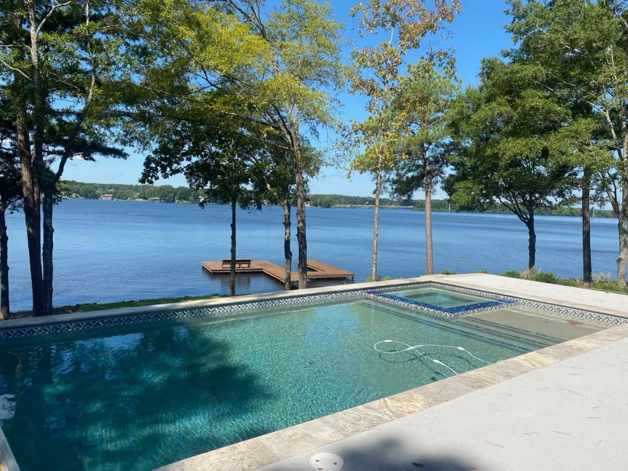 Swimming pool overlooking a lake, blue water, trees, dock, sunny day.