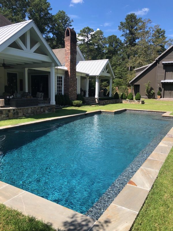 Pool with blue water, stone coping, and two covered patios with white gables in a grassy yard.