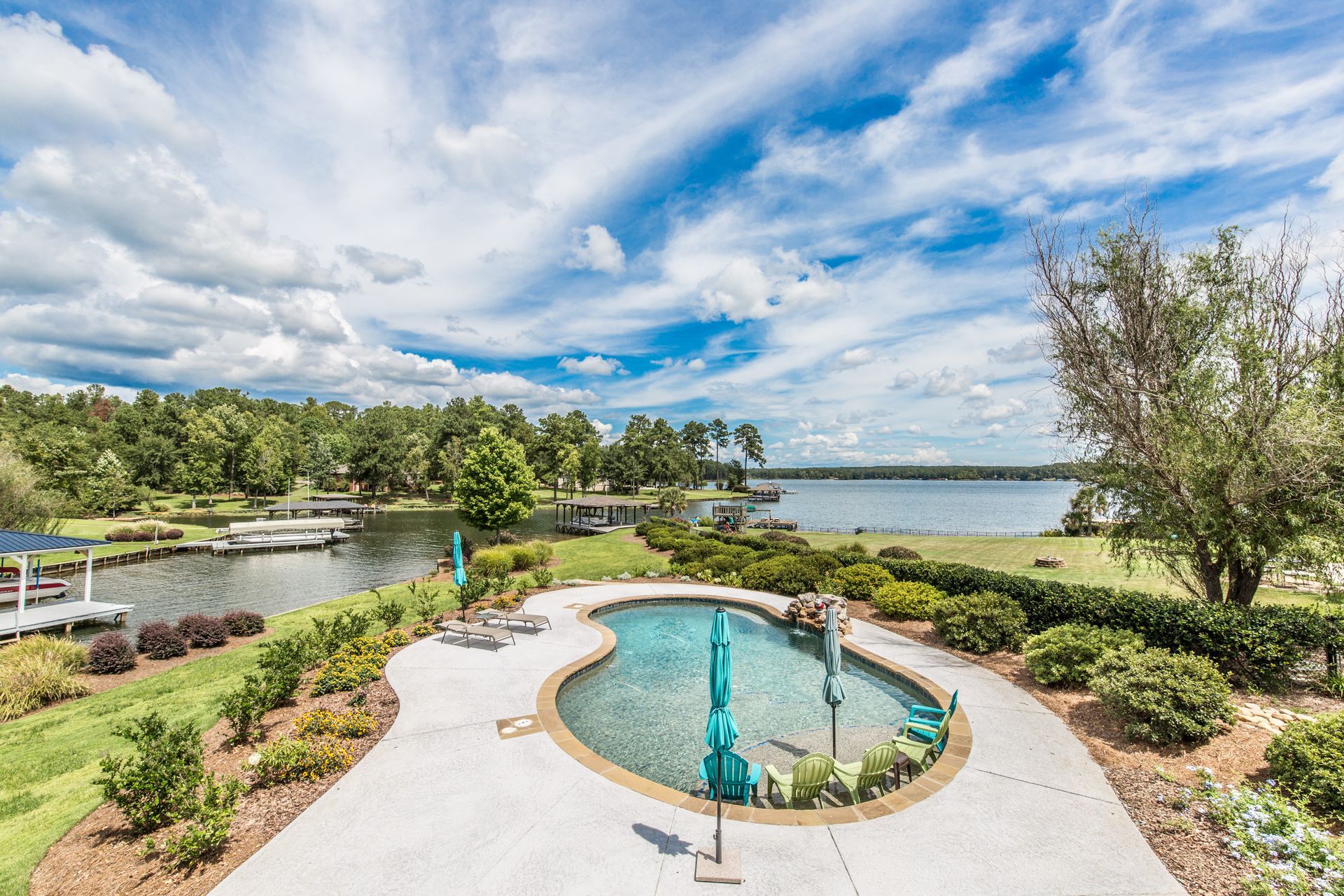 Pool overlooking a lake, surrounded by greenery under a blue sky with clouds.