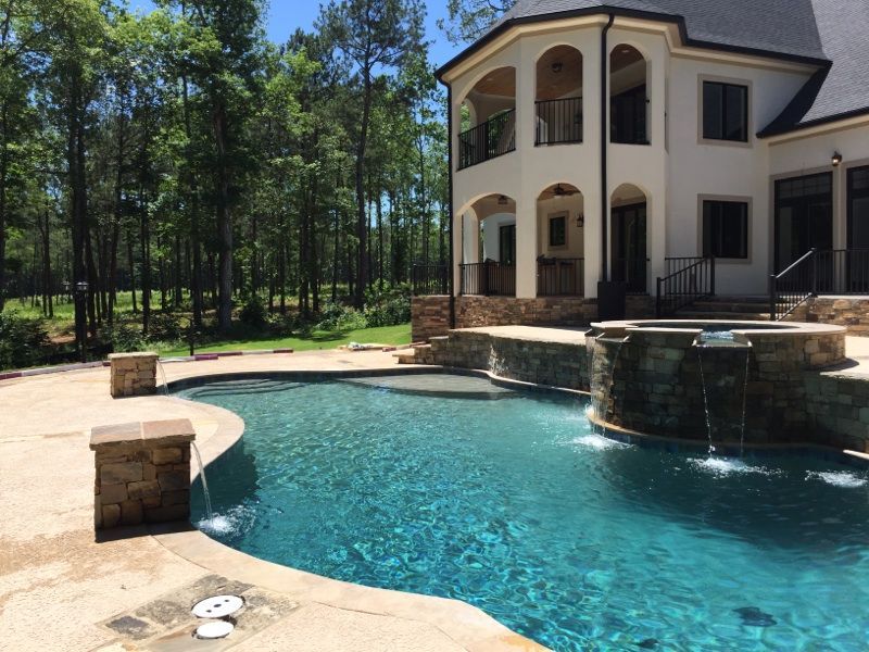 A luxury home with a pool. The pool is surrounded by a stone patio, with a forest backdrop.