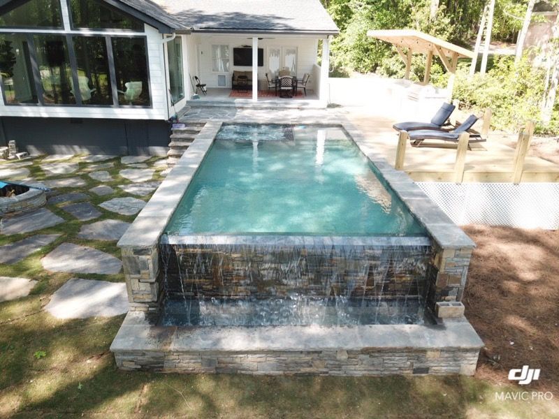 Rectangular pool with waterfall feature and stone surround, backyard setting.