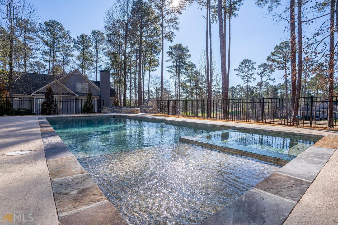 Swimming pool with stone border, surrounded by trees. House visible in background.