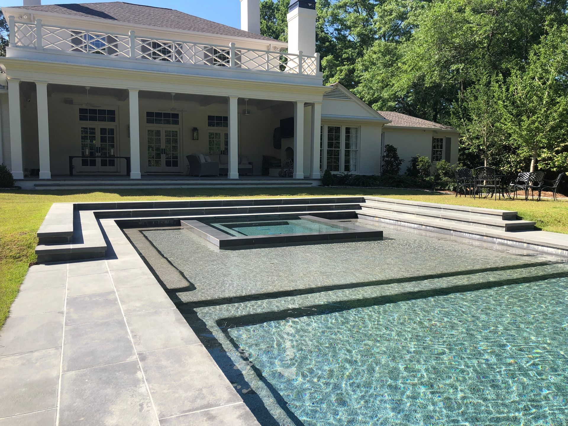 Swimming pool and spa next to a white house with columns and a balcony.