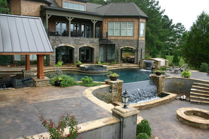 Large house with a pool, waterfall, and patio. Stone facade and outdoor seating.