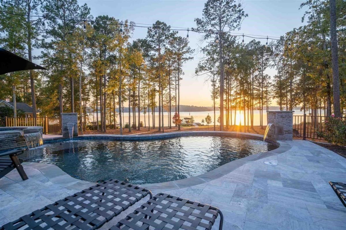 Pool overlooking lake at sunset, trees in background, lounge chairs in foreground.