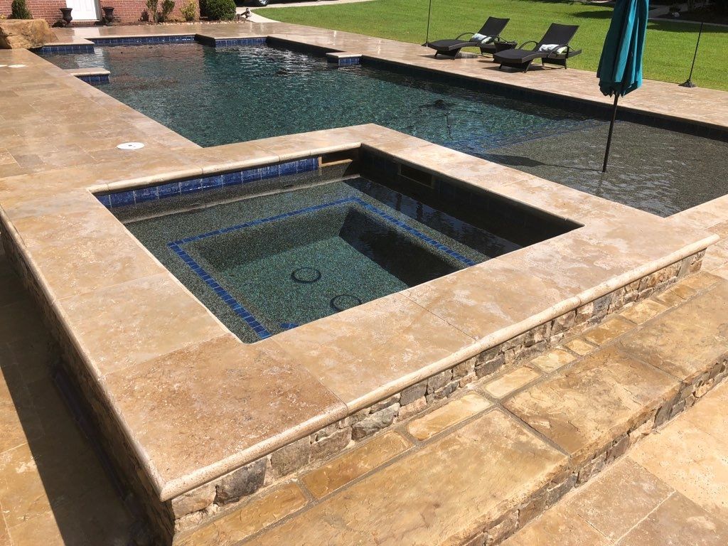 A backyard pool with a spa, surrounded by stone patio.