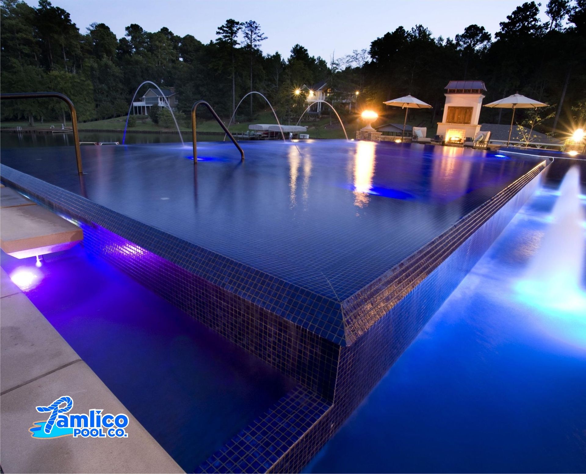 Blue-lit infinity pool with water fountains, night setting.