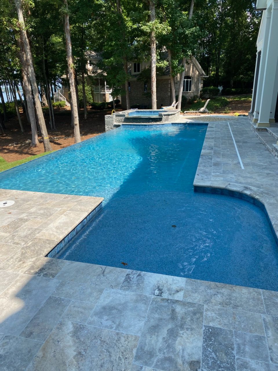 Swimming pool with blue water and stone patio, hot tub, and trees.