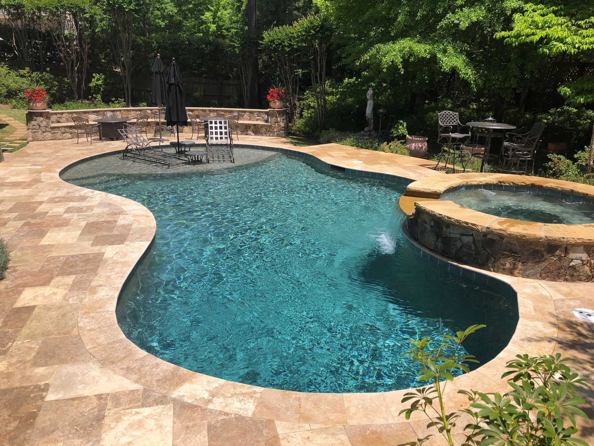 Swimming pool with a spa surrounded by stone, with lounge chairs and a dining set.