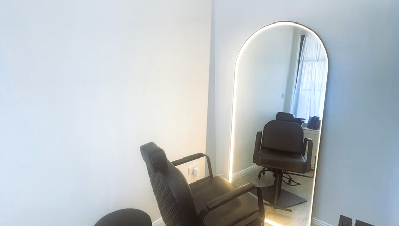 Minimal beige salon with a white chair, vanity mirror, and plants in soft natural light