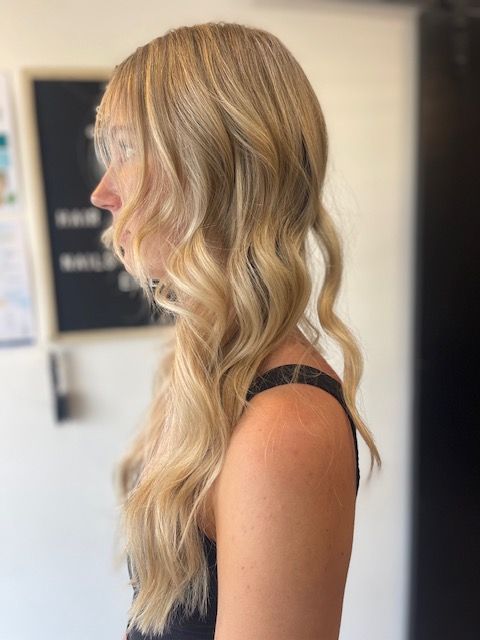 Side profile of a woman with long wavy blonde hair in a black top indoors