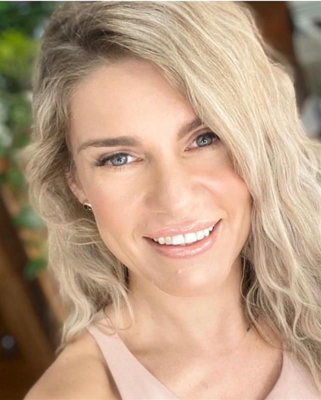 Close-up portrait of a smiling person with wavy blonde hair and a light pink top