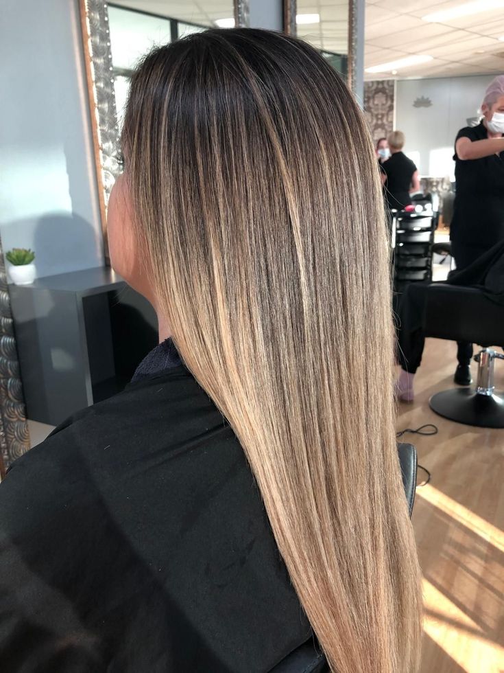 Long straight ombré hair from dark roots to blonde ends in a salon setting