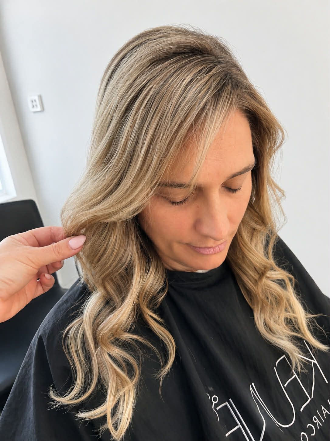 Woman with wavy blonde hair getting her hair adjusted in a salon chair