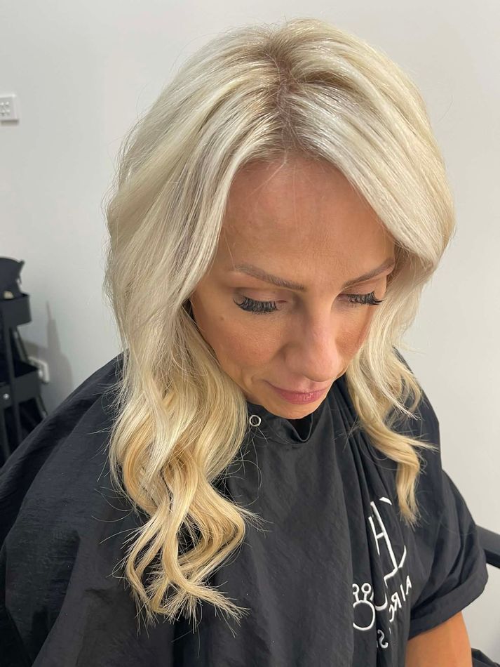 Woman with blonde wavy hair looking down, wearing a black salon cape indoors