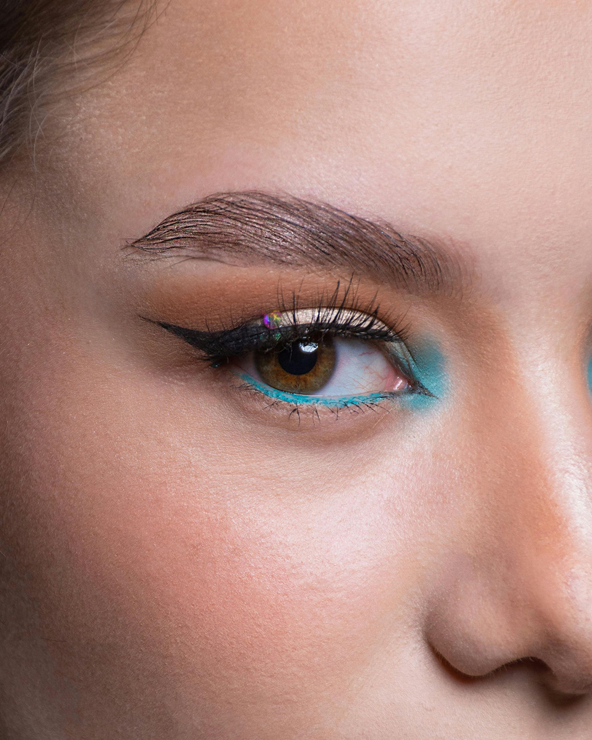 Close-up of a face with turquoise eyeliner and winged brown eye makeup