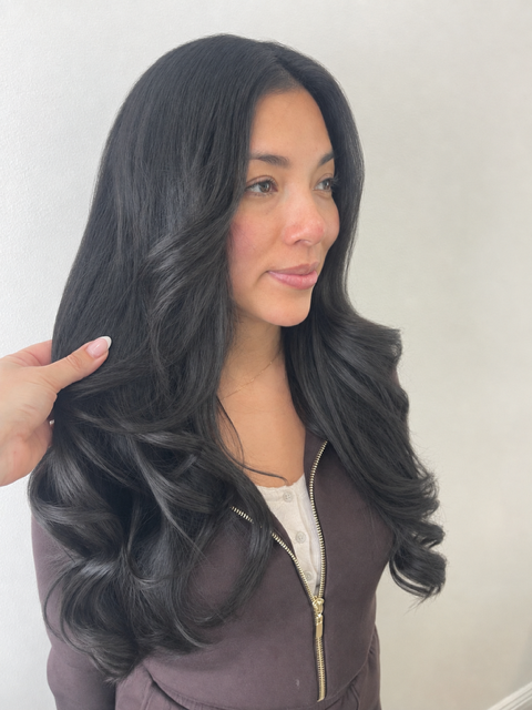 Woman with long black hair in a dark jacket, shown in profile against a plain light background.