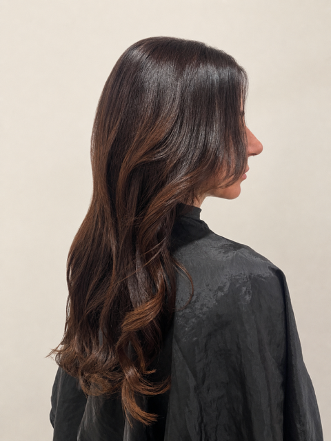 Side view of a woman with long wavy brown hair wearing a black top against a plain background