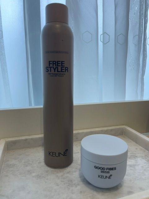 Gray hair spray can and white cream jar on a tray by a window.