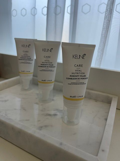Three skincare tubes on a white tray by a window with sheer curtains