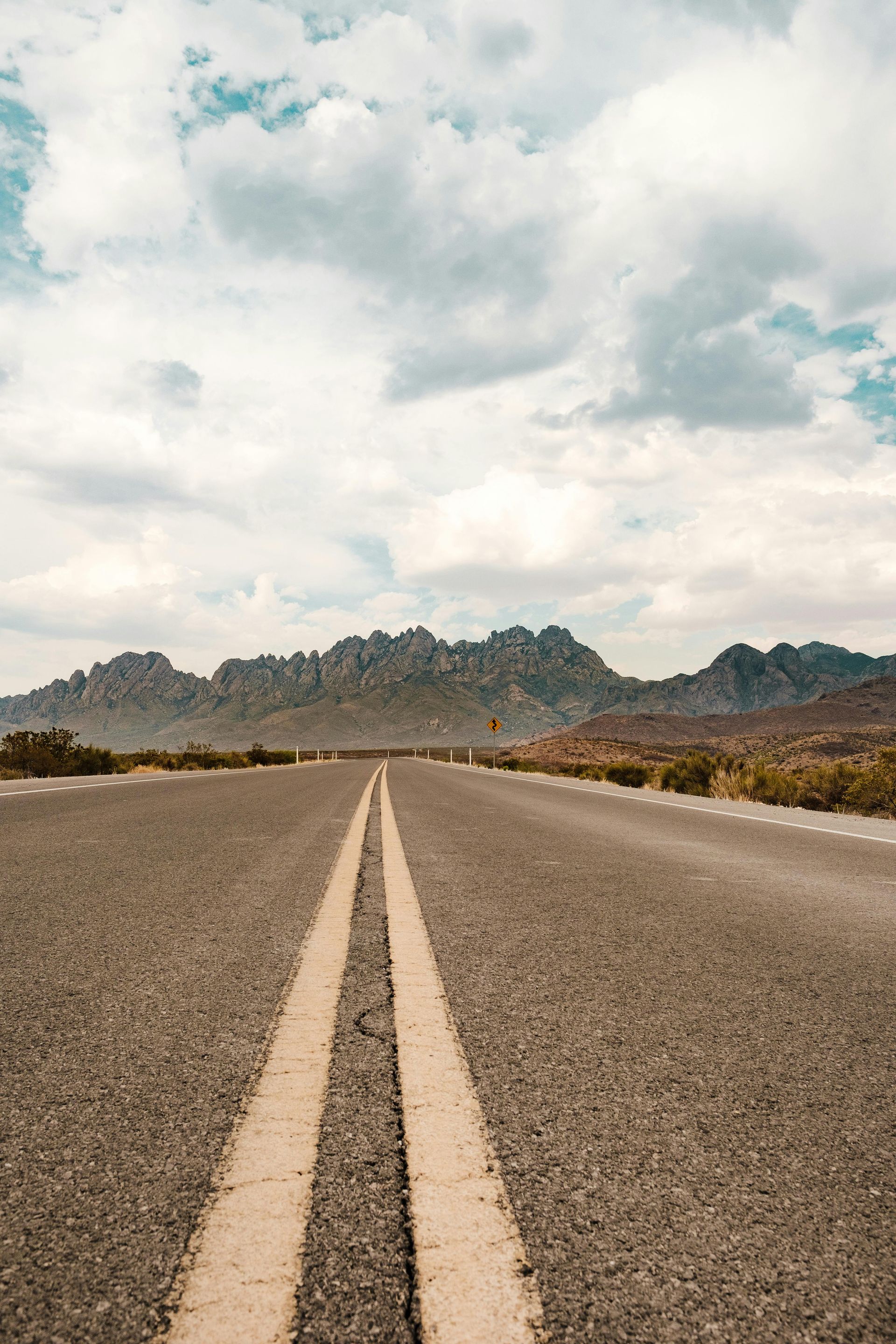 A road going through a desert with mountains in the background.