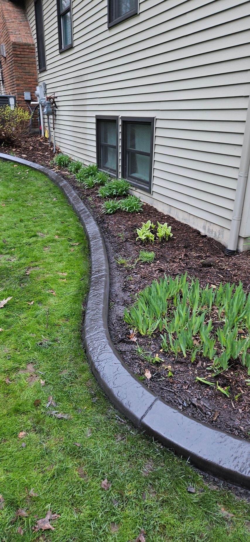 Curved stone border edging a mulched garden bed along a house with gray siding and small shrubs