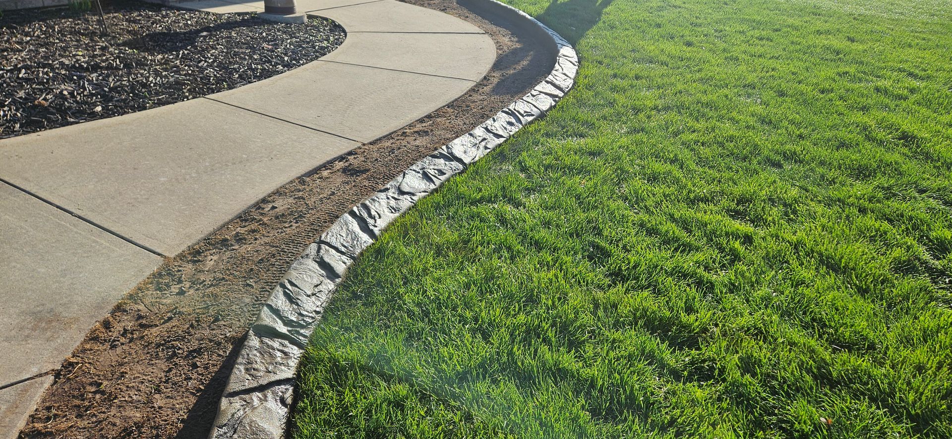 Curved stone walkway beside bright green grass in a landscaped garden