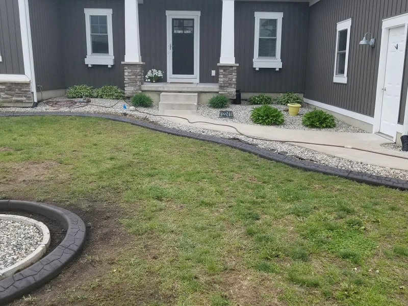 Dark gray house exterior with a concrete walkway, landscaping rocks, and a curved decorative concrete lawn border.