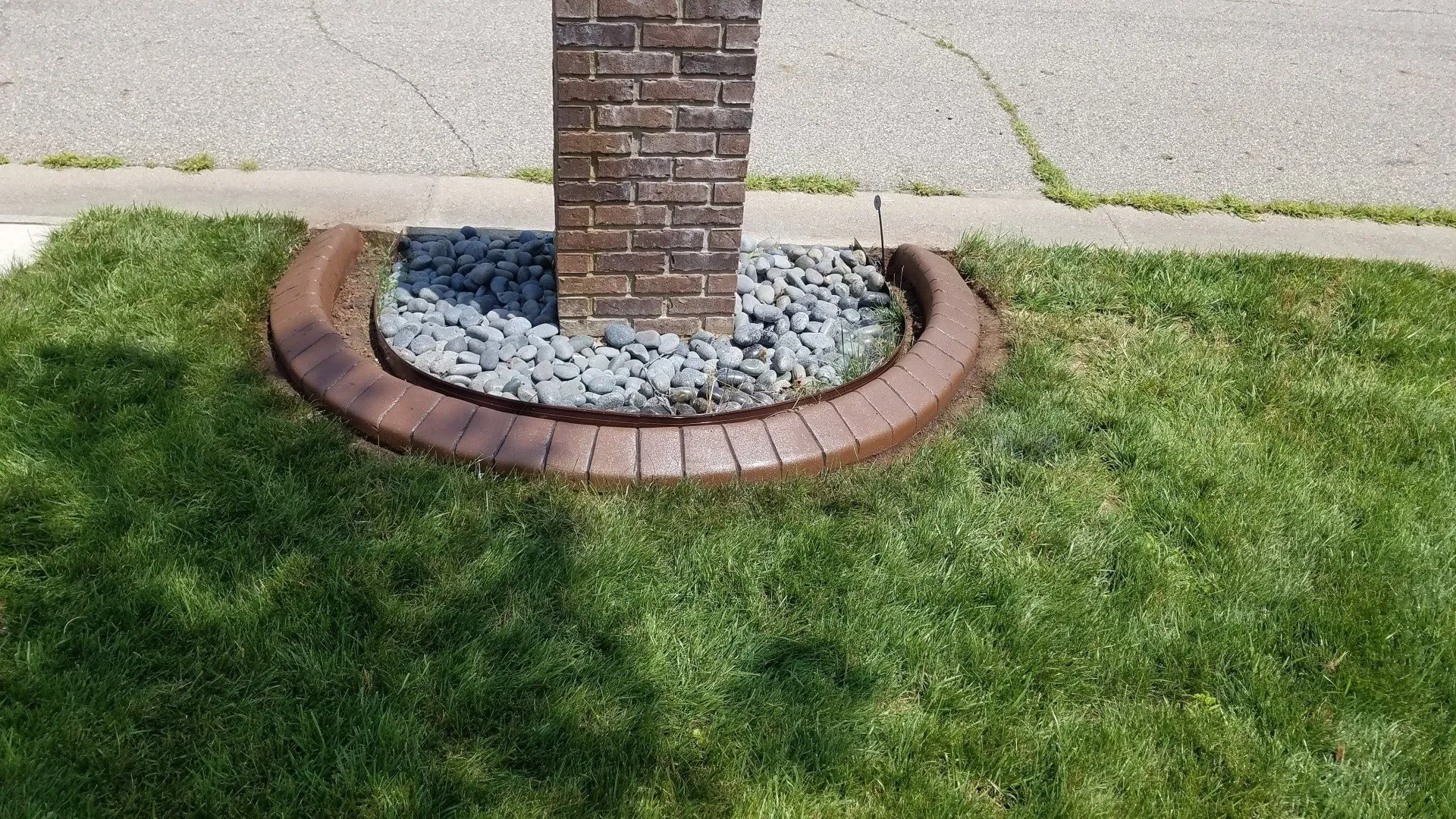 A brick mailbox post surrounded by grey decorative rocks and a curved brown concrete landscape border set in a lawn.