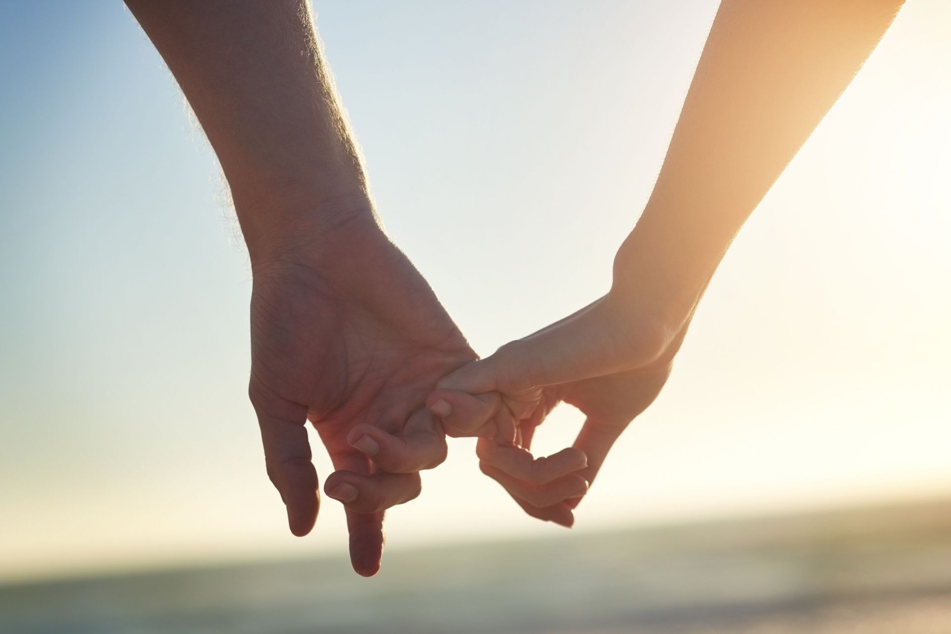 Two hands holding pinkies together against a bright sunset sky