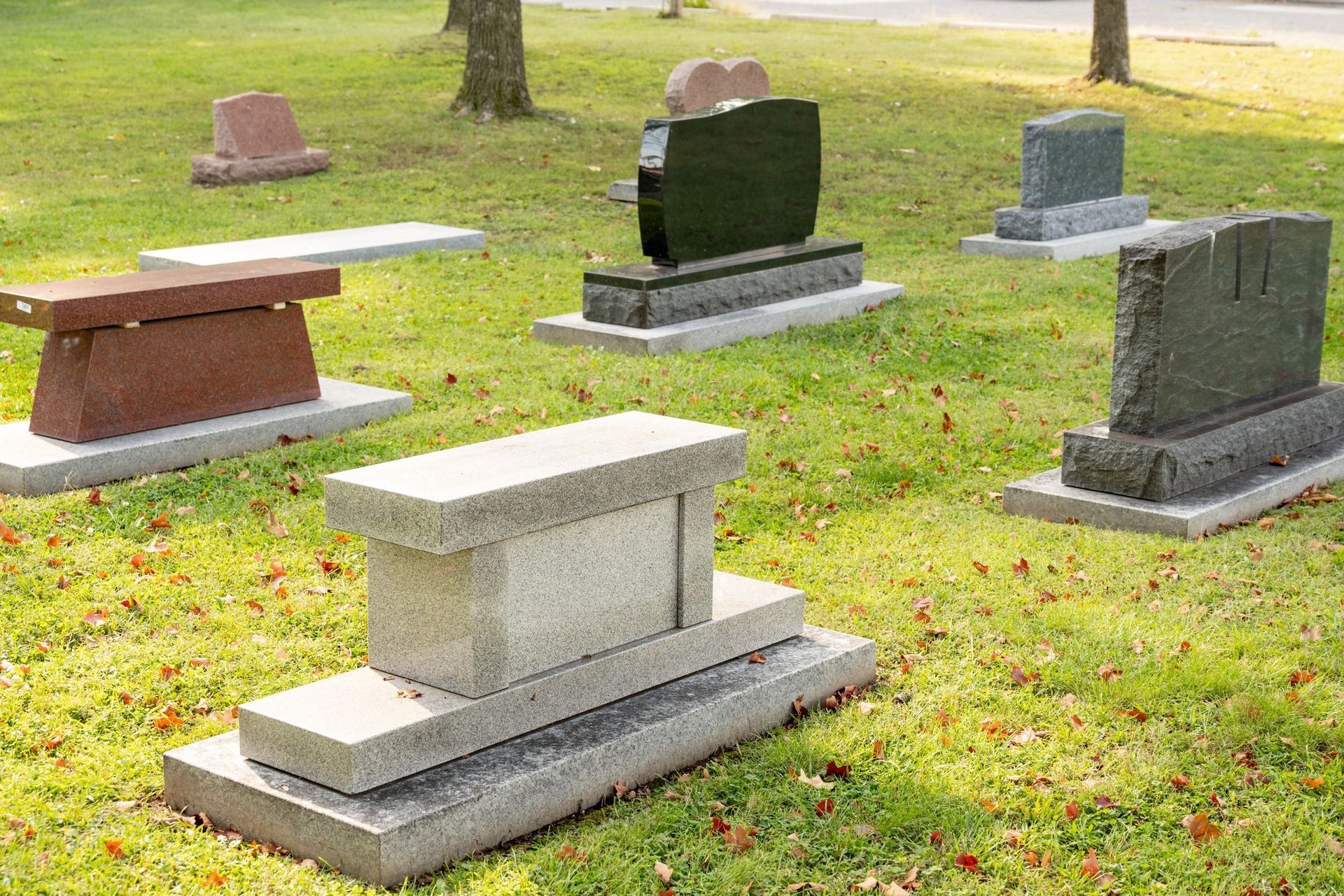 Several gravestones in a grassy cemetery, including a white tombstone in the foreground.