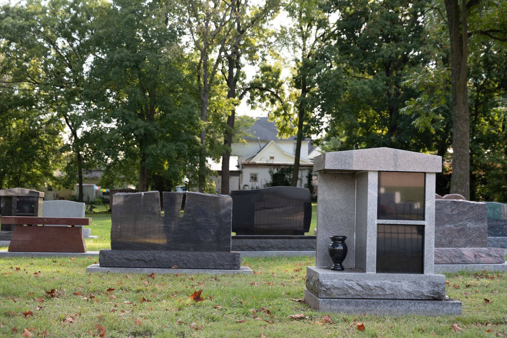 Stone memorials in a tree-lined cemetery, including a small gray monument in the foreground