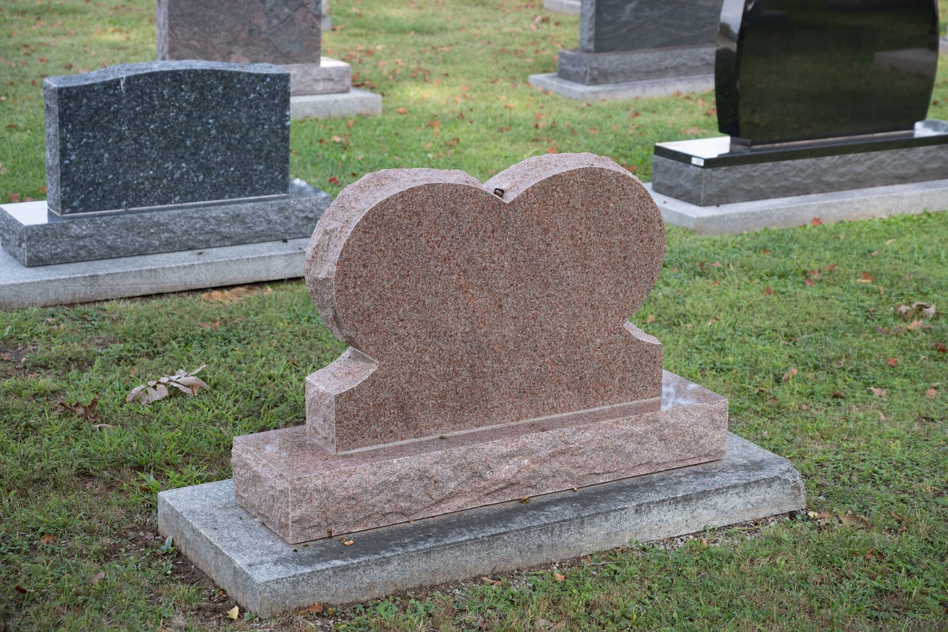 Pink granite gravestone in a cemetery with other headstones in the background