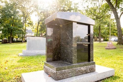 Black granite memorial monument on a white base in a sunny cemetery park.