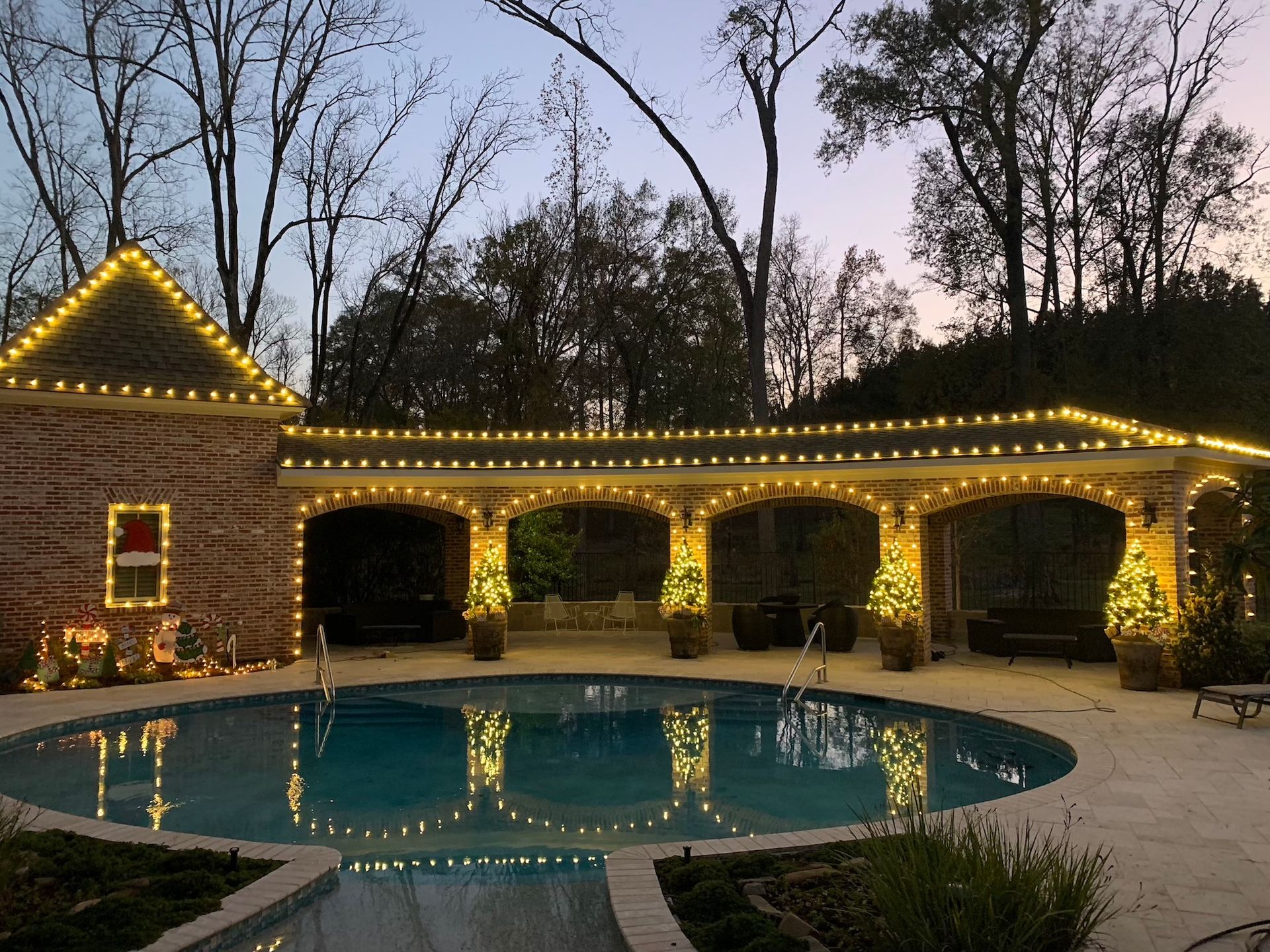 A large swimming pool is surrounded by christmas lights.