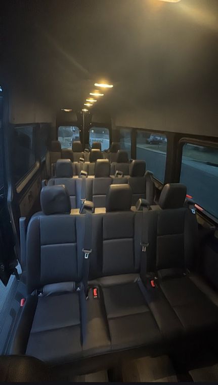 Interior of a passenger van with rows of dark gray seats and overhead lights.