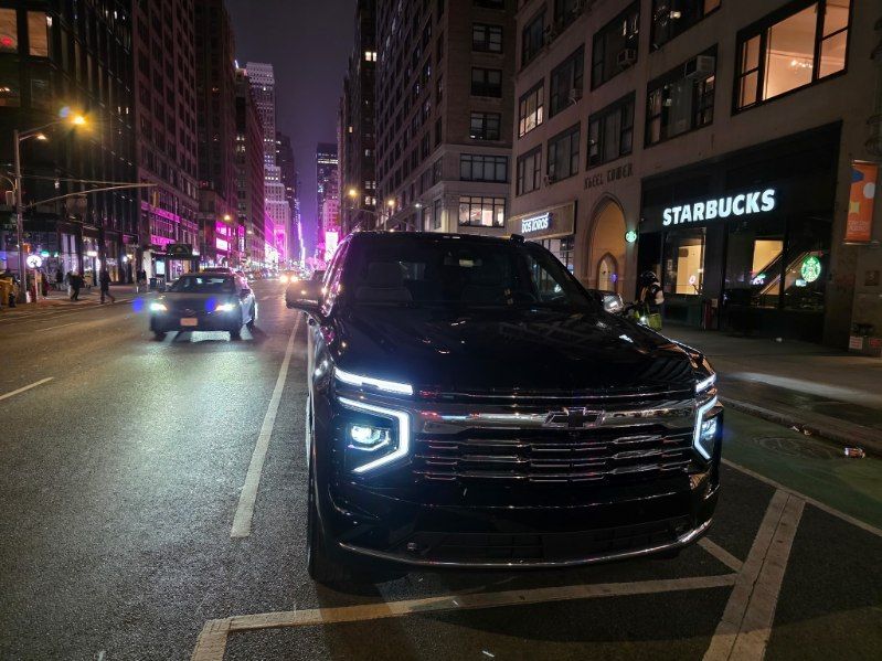 Black SUV parked on a city street at night, with a Starbucks in the background. Buildings and streetlights.