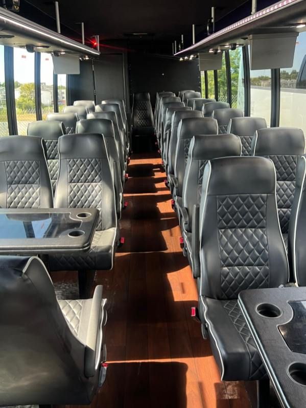 Interior of a bus with rows of black leather seats, tables, and a wooden floor.