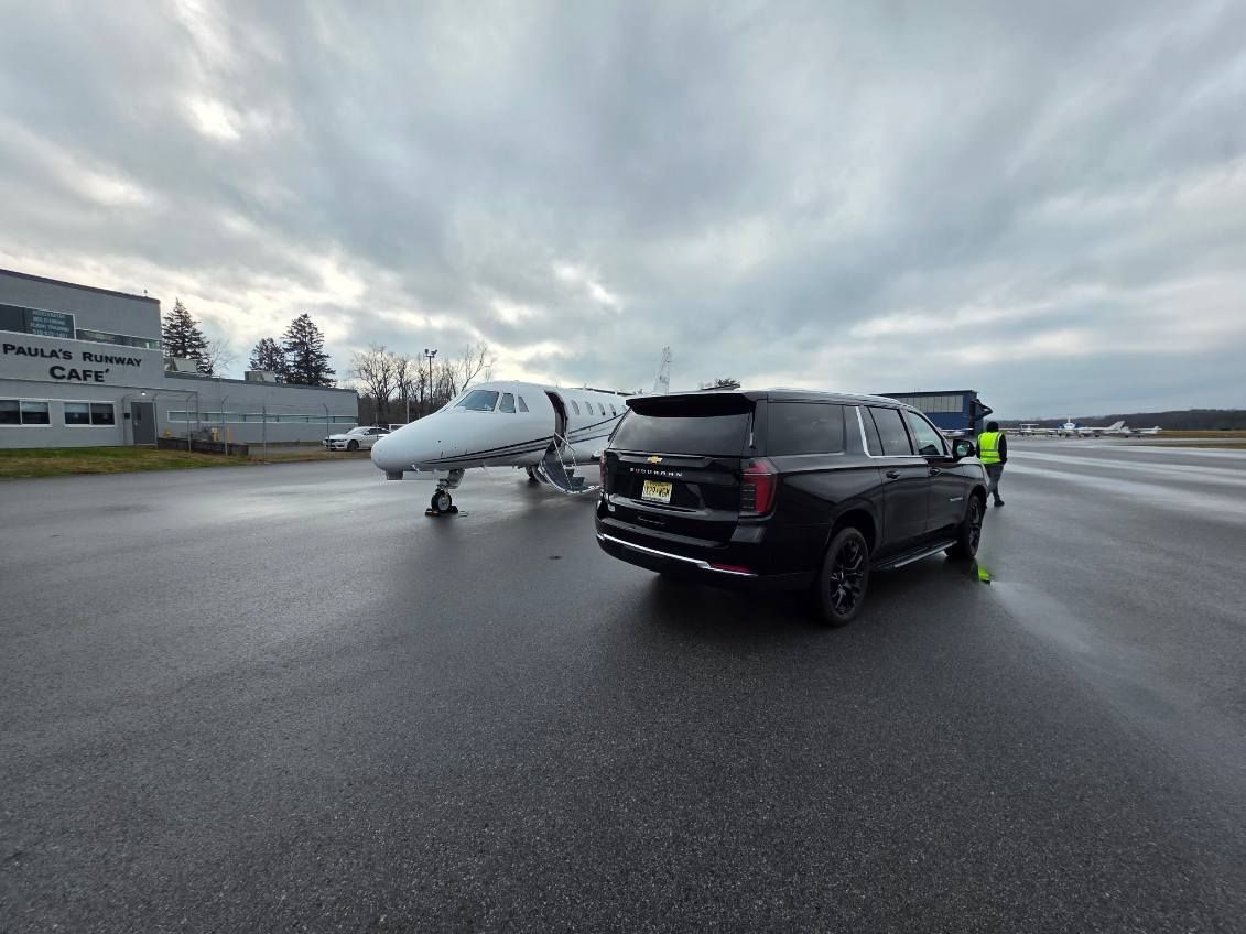 A black SUV next to a private jet on a wet tarmac under a cloudy sky.