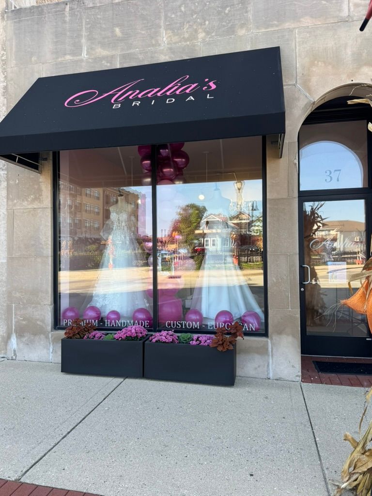 Storefront with black awning and pink lettering, display window, and sidewalk outside a shopping center
