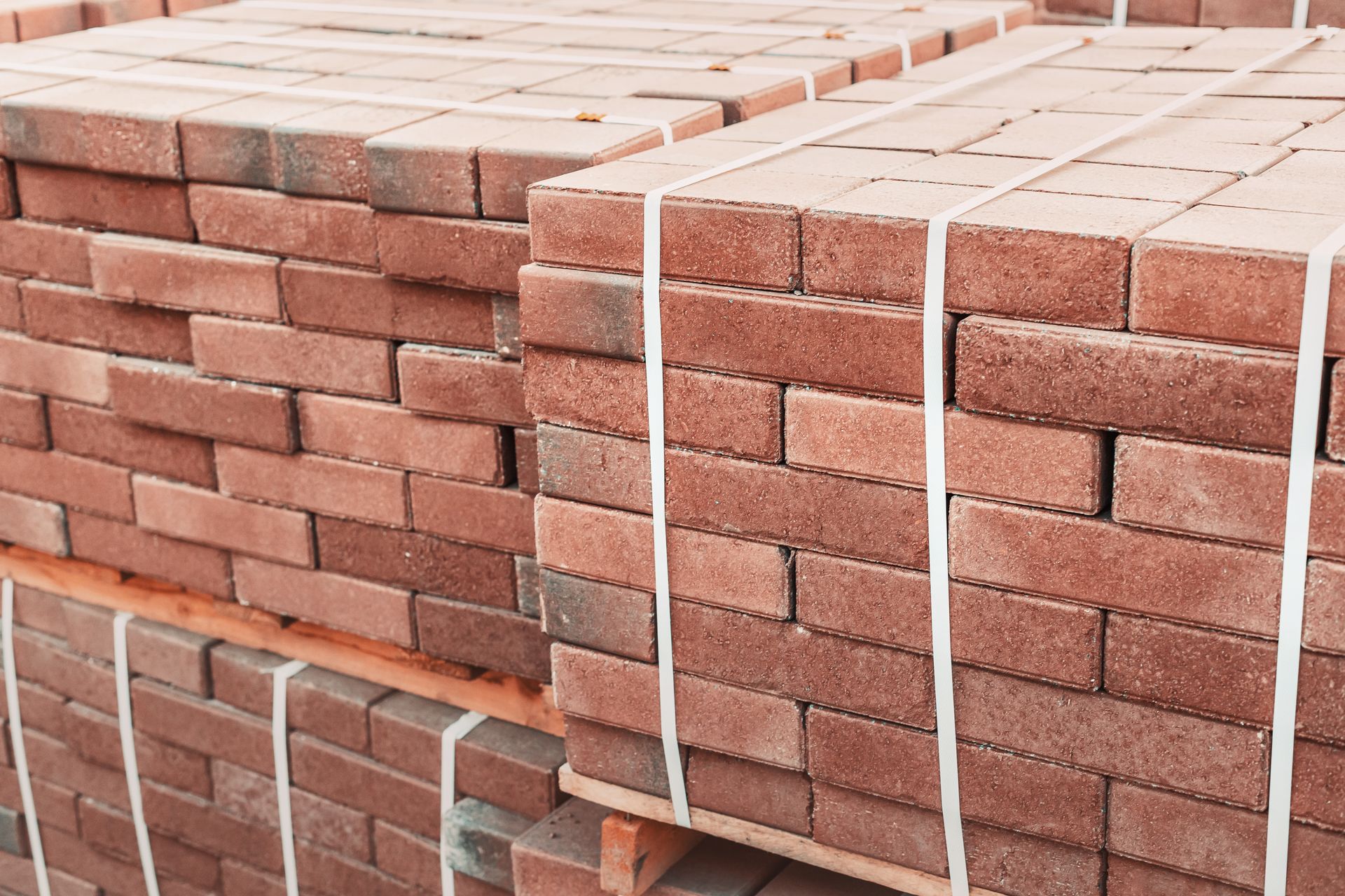Stacked pallets of red bricks wrapped in white banding straps, ready for delivery