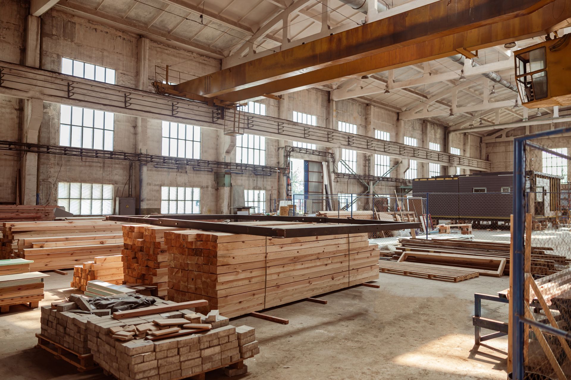 Lumber warehouse interior with stacked wood planks, overhead crane, and industrial storage facility.