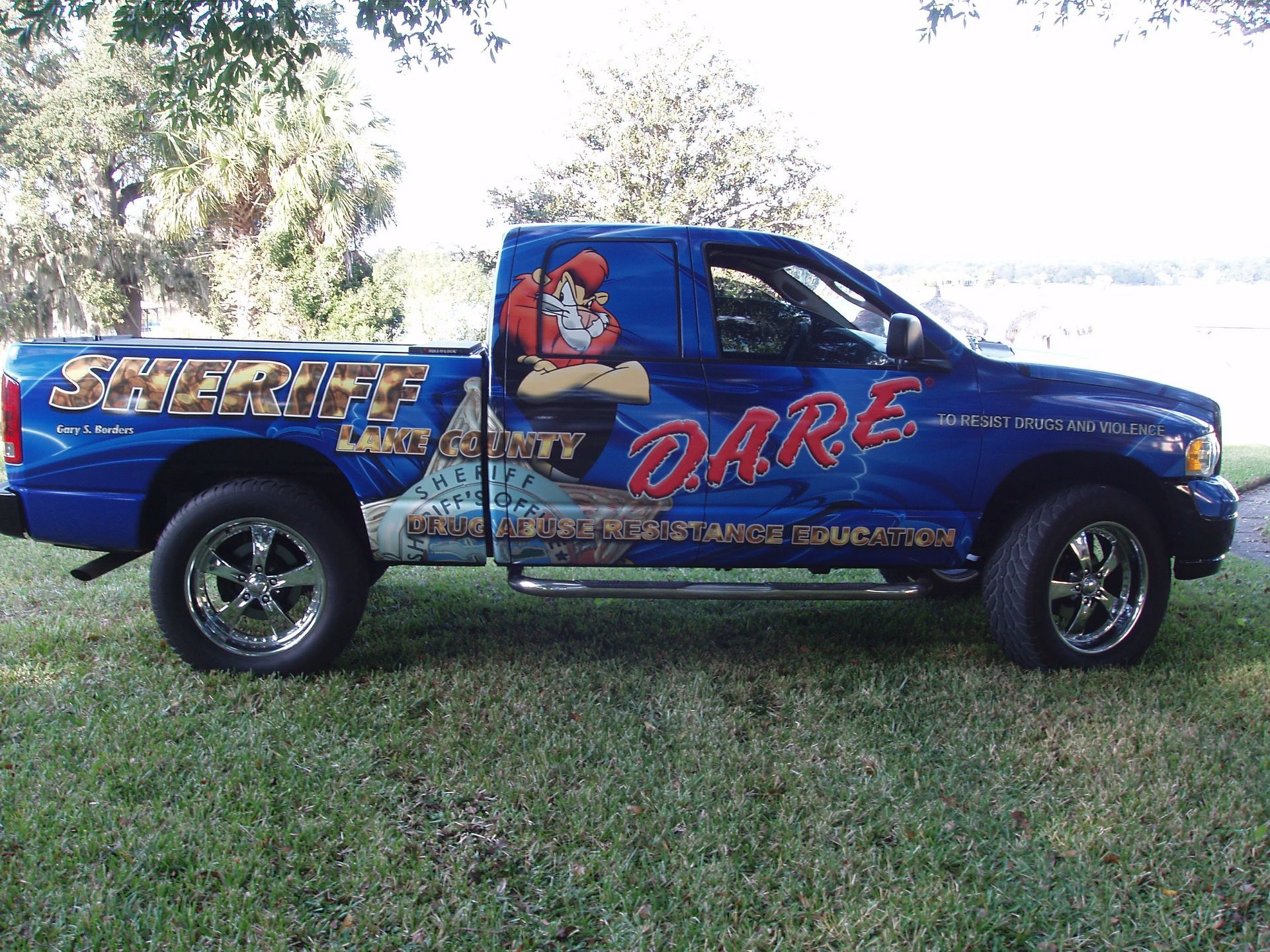 Blue Sheriff DARE truck with cartoon graphic, parked on grass.