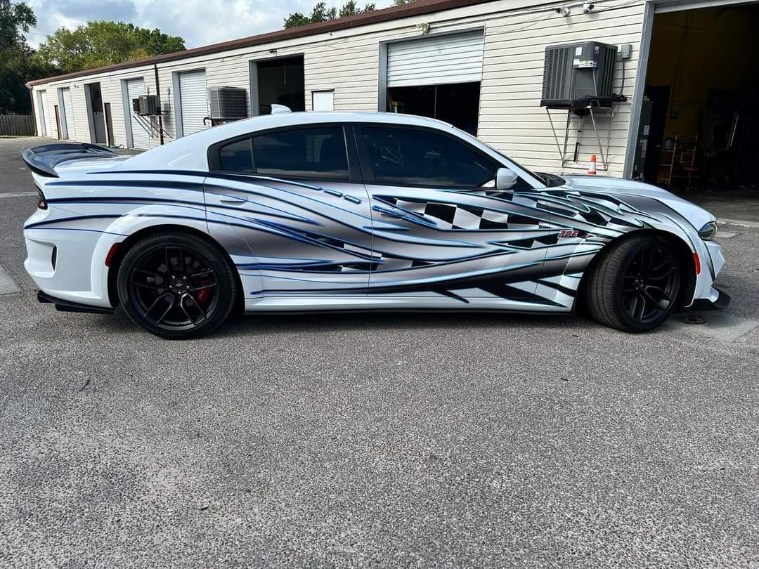 White Dodge Charger with black wheels and a custom black and blue graphic wrap parked outside a building.