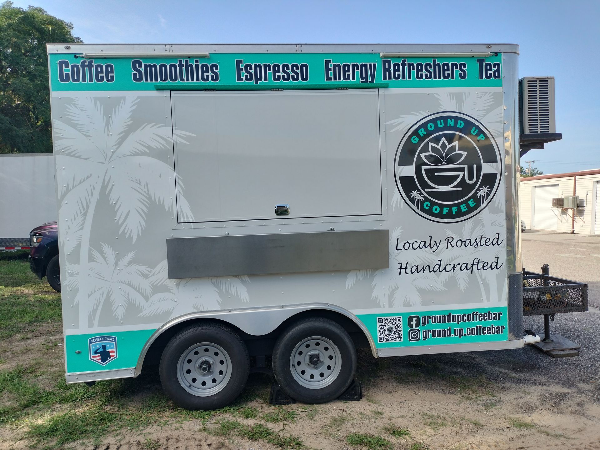 Coffee trailer with palm trees and logo, serving coffee, smoothies, and tea.