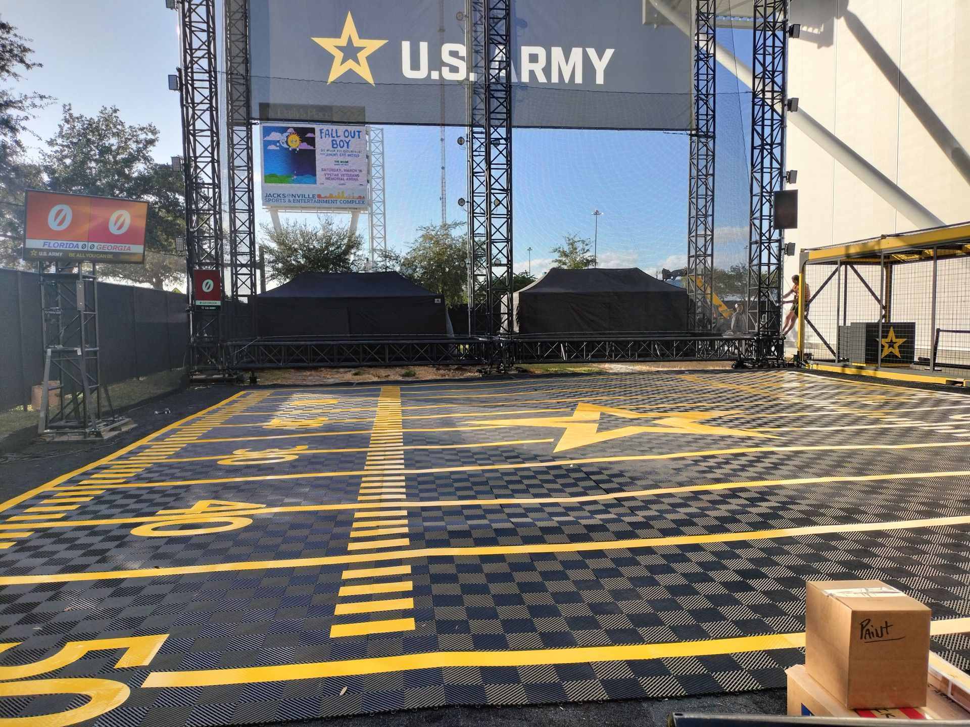 An outdoor U.S. Army event area with black and yellow flooring, two black structures, and a banner.