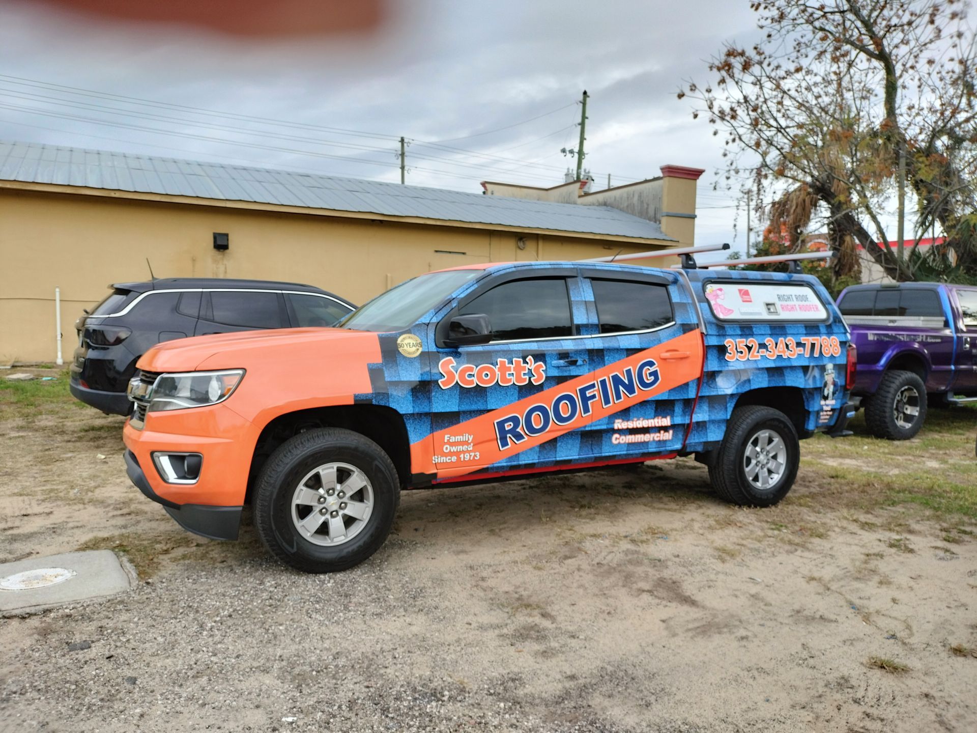 A roofing company truck with orange and blue wrap, parked in a lot. 