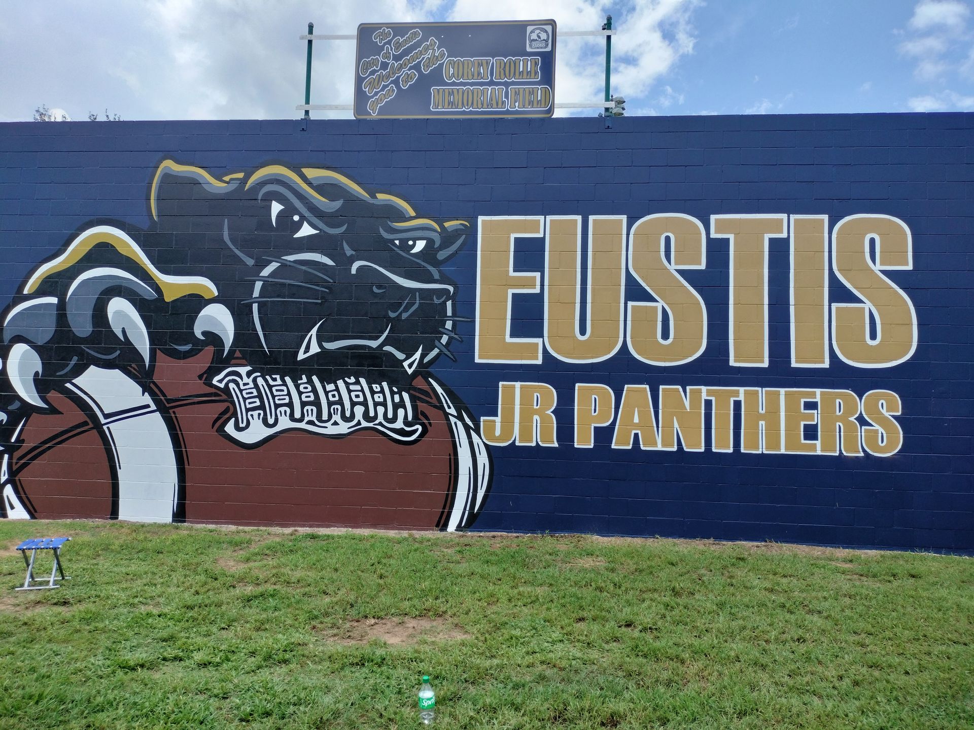 Mural of a black panther mascot holding a football, Eustis Jr. Panthers text on a blue wall.
