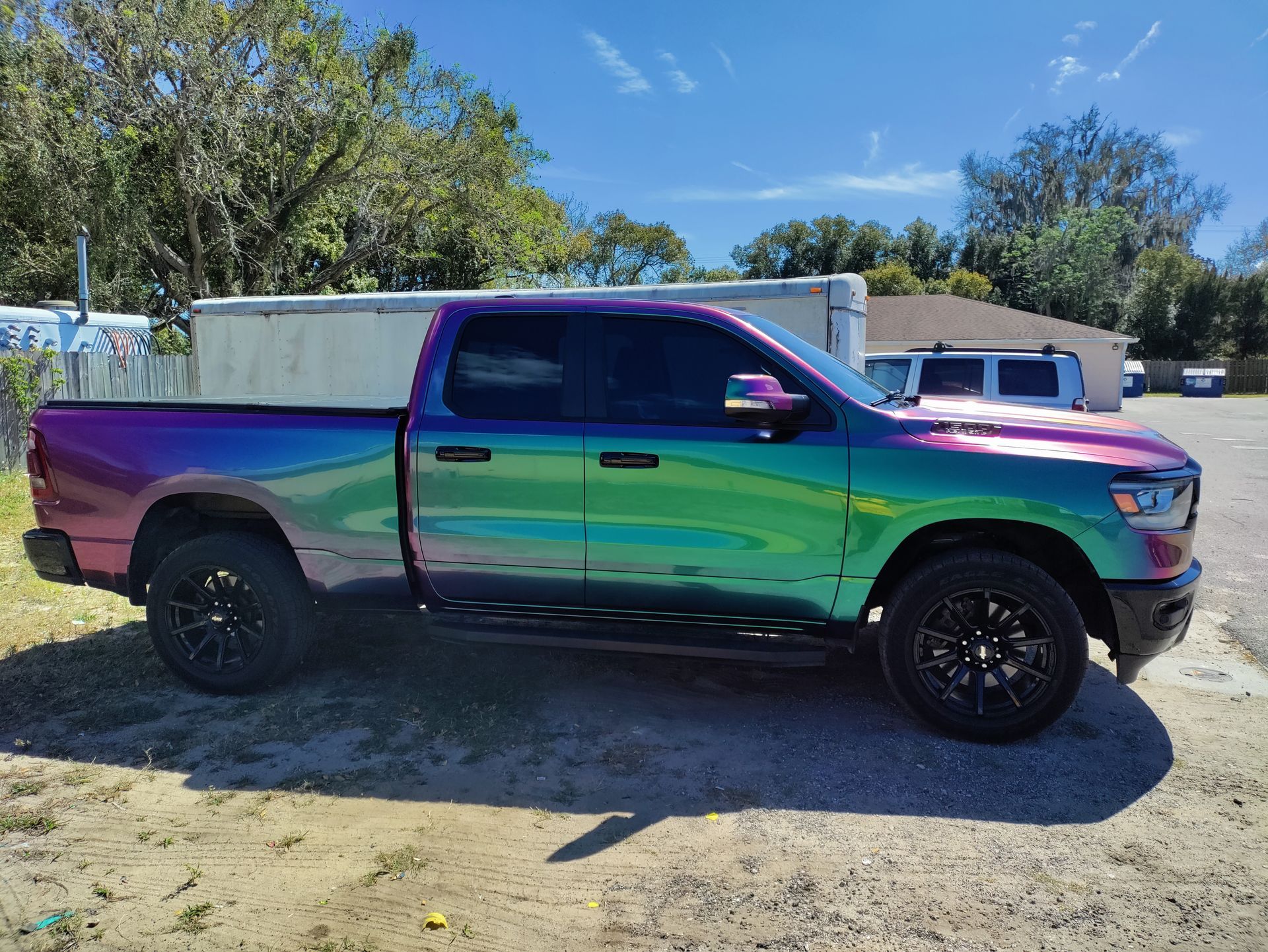 Ram pickup truck with iridescent wrap, black wheels, parked outside on a sunny day.